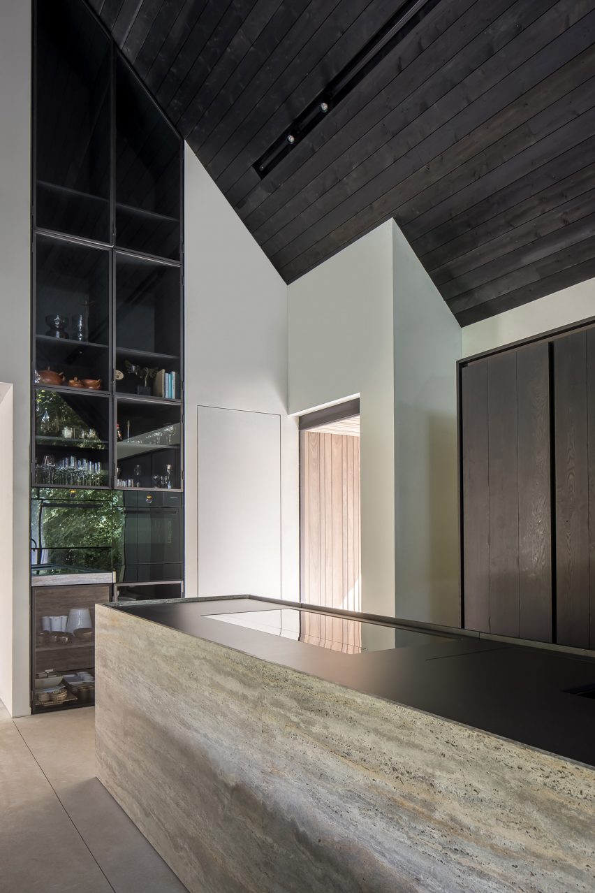 Kitchen interior with a stone island, white walls and dark pitched timber ceiling