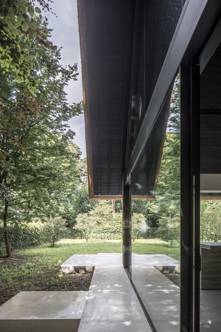 Glazed exterior of Villa VD with paved terrace in a lush garden