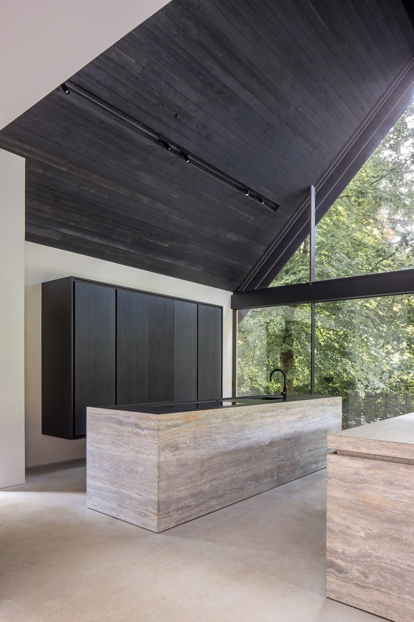 Kitchen interior with a stone island, white walls and dark pitched timber ceiling