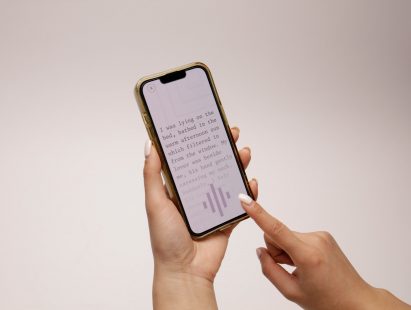 Photo of a person scrolling some text on a smartphone. The text reads "I was lying on the bed, bathed in the warm afternoon sun which filtered in from the window. My lover was beside me, his hand gently caressing my neck. Suddenly, I felt..."