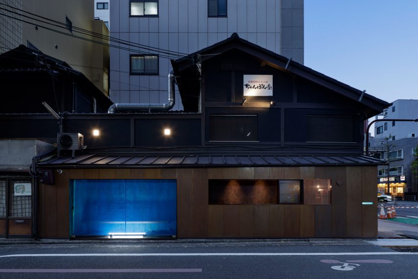 Blue oxidised copper kiosk along a black timber building by G Architects Studio
