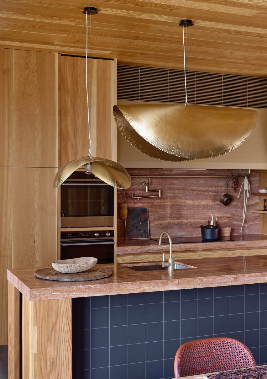 Kitchen with wood-lined ceiling, wall cupboards, island and gold pendant lamp shades