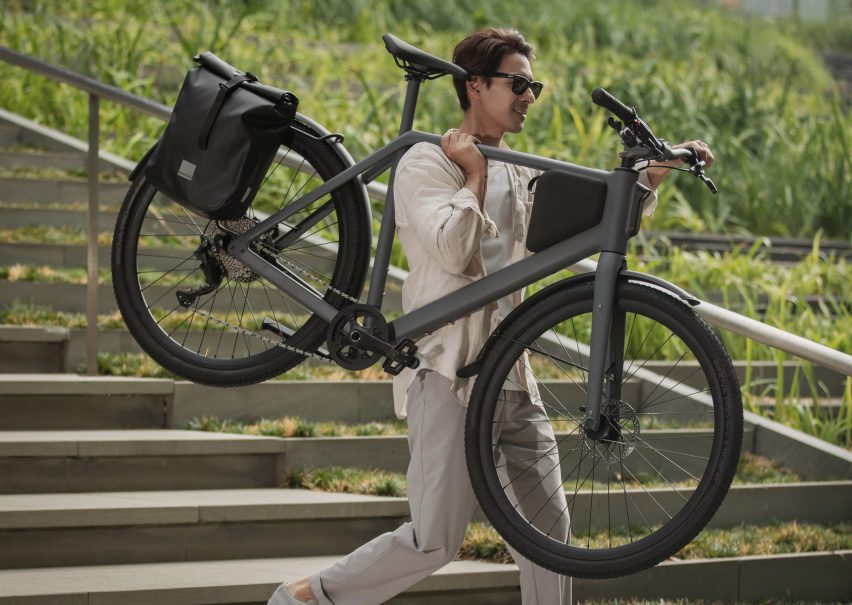 Photo of a youthful man in sunglasses carrying a Lemmo One bike on one shoulder as he walks down a set of steps outdoors