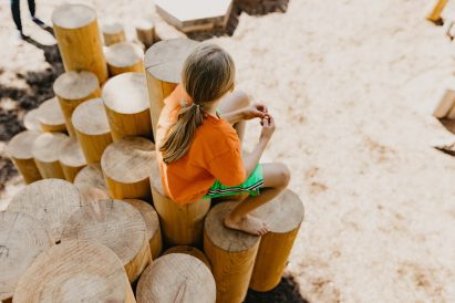 A kid sitting on a structure made of vertical ogs