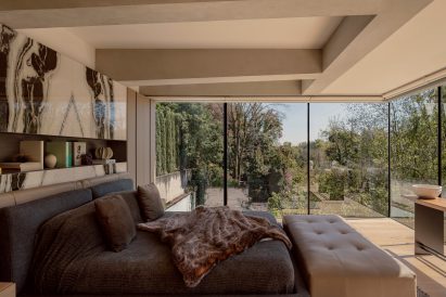 Bedroom with dark bedding and floor-to-ceiling windows giving views to a garden