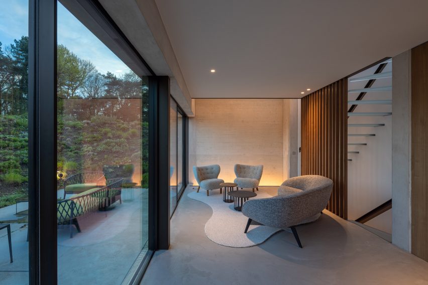 Concrete living room with lounge chairs and floor-to-ceiling glass doors leading to a patio