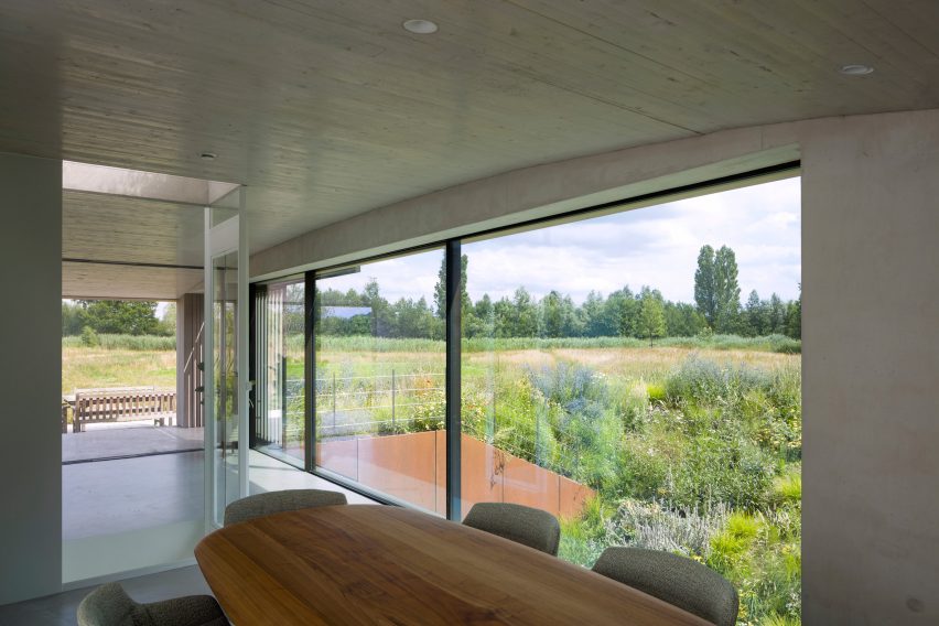 Concrete dining room with large windows overlooking a grassy landscape