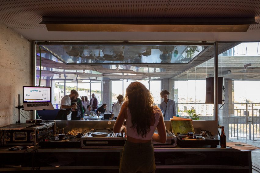 Photo of the inside of a DJ booth, looking out onto a cafe-like space where people mingle with drinks