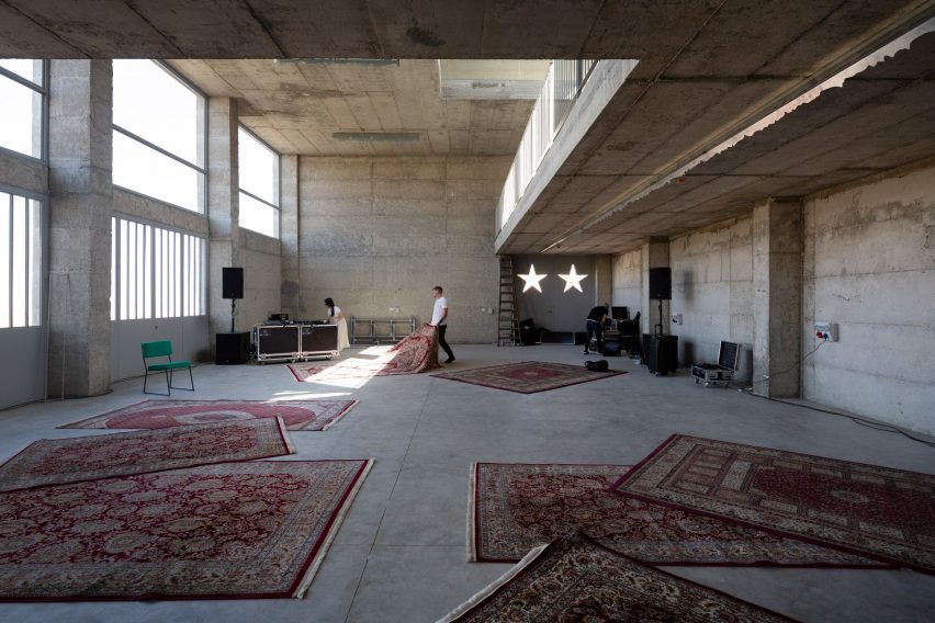 Photo of the basement level of The Wonder Cabinet, showing a large open space with large windows on one wall, an opening cut into the slab above and rugs strewn over the top