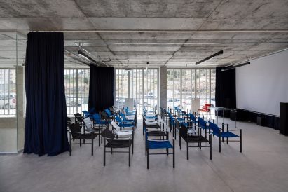 Photo of a simple function room in an open concrete room with chairs arranged in rows, a screen in the front, and curtains on rails around the space
