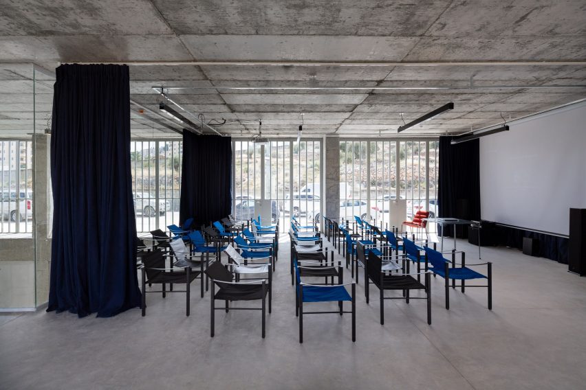 Photo of a simple function room in an open concrete room with chairs arranged in rows, a screen in the front, and curtains on rails around the space