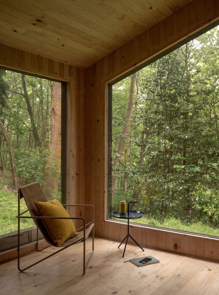Interior of a timber cabin with large windows looking onto a forest