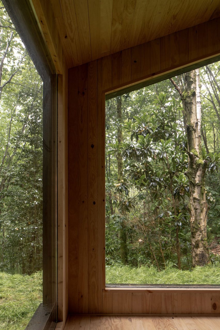 Interior of a timber cabin with large windows looking onto a forest