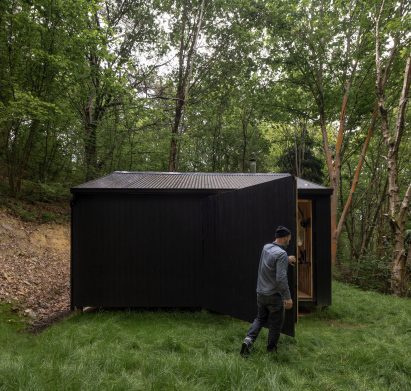 Man closing door of black woodland cabin