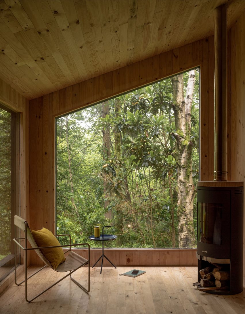 Interior of a timber cabin with large windows looking onto a forest