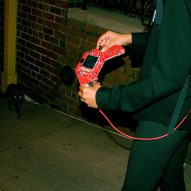 A person holding a red device with a cat in corner