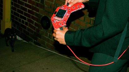 A person holding a red device with a cat in corner