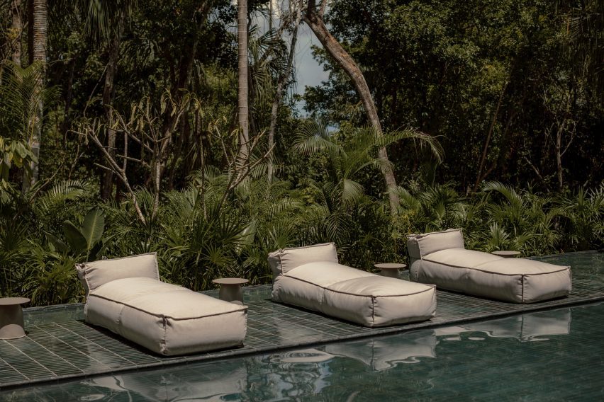 A pool in a jungle with cushion lounge chairs