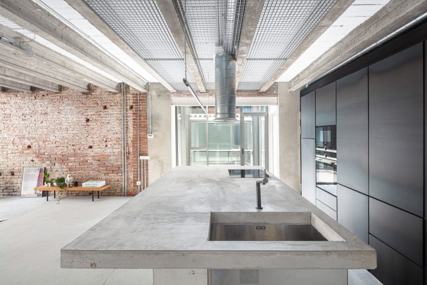 Kitchen with a brick wall, exposed ceiling beams and a concrete island