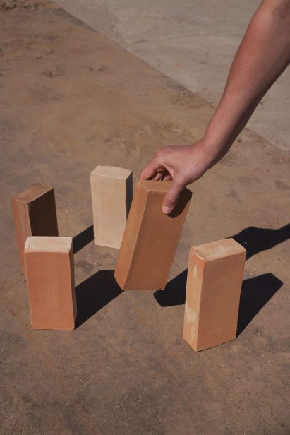 Photo of a hand reaching out from edge of frame right to grab a brick from five on the ground