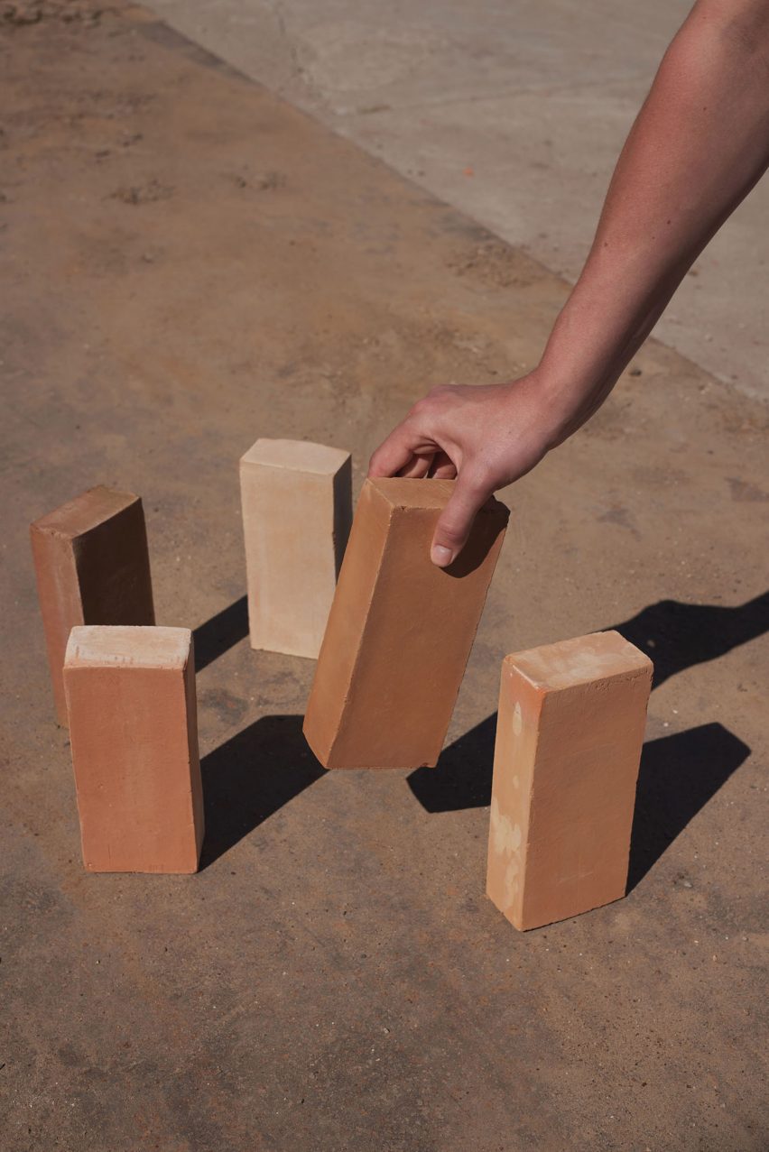 Photo of a hand reaching out from edge of frame right to grab a brick from five on the ground