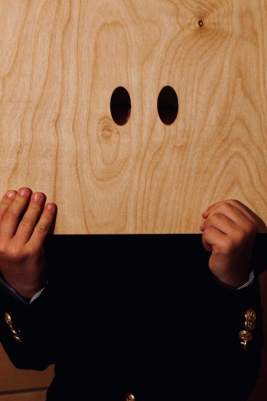 A kid looking through eyes-holes cut into plywood