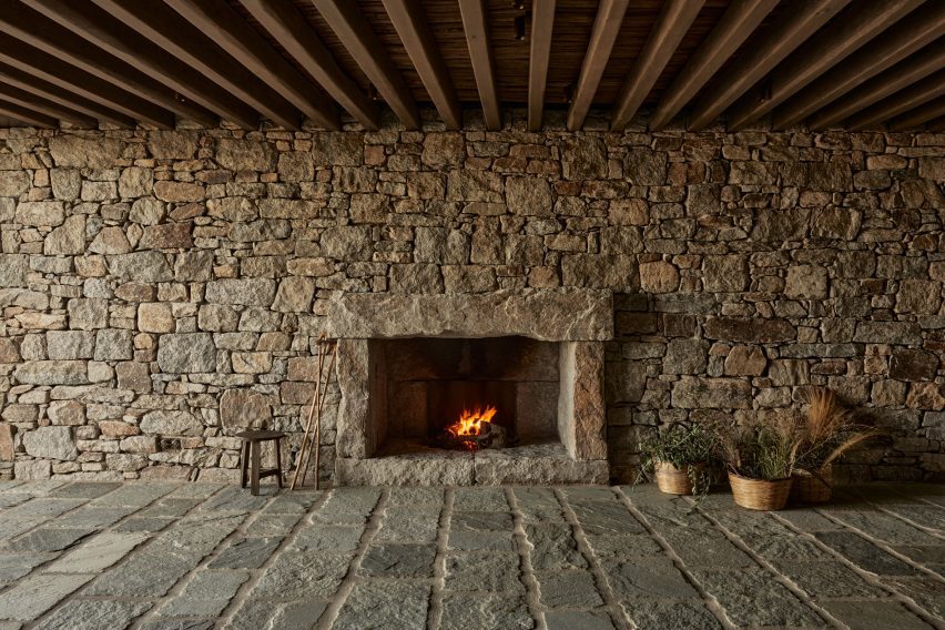 Room with stone walls and floors, timber ceiling beams and a fireplace
