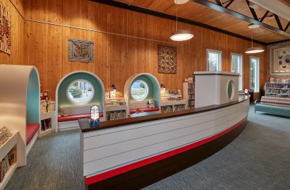 A children's corner of a library with light blue shelving and little chairs and boat