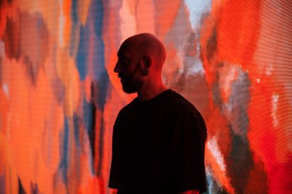 Headshot of the artist Quayola in shadow with his head held close to one of his artworks