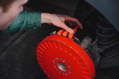 Close-up photo of designer Alex Burton fitting the REVR prototype onto a car's rear disc brakes