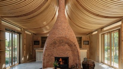 Strips of wood curve from the ceiling, while a central brick fireplace divides the open space