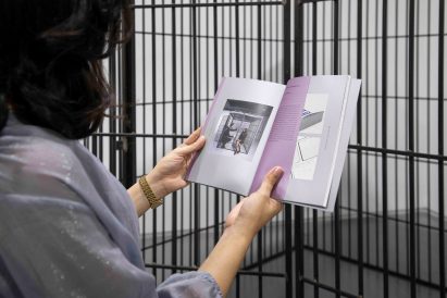 Photo of someone holding an exhibition booklet in front of a metal cage