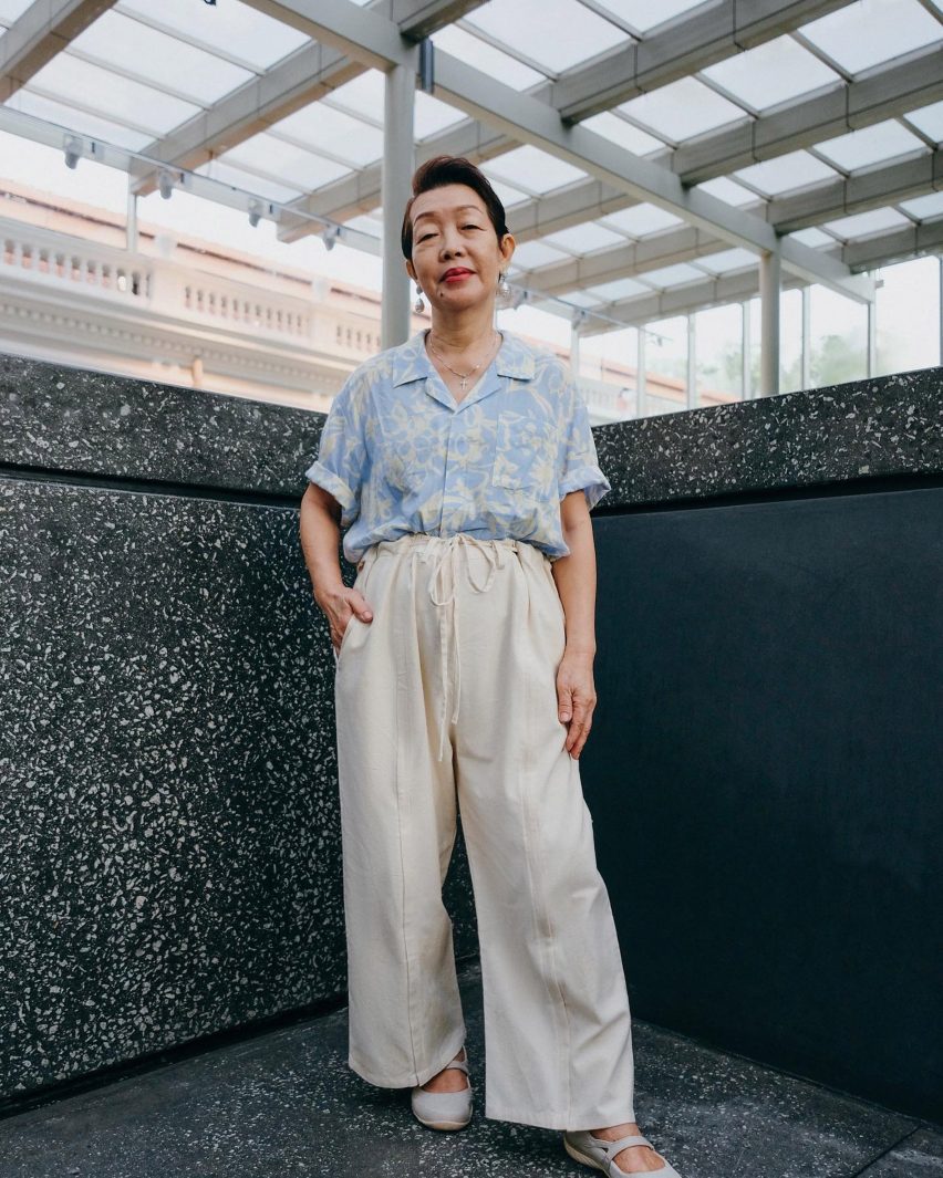 Photo of an elegant older model wearing a tropical-print light blue shirt and light beige trousers by Will&Well