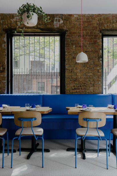 Pendant light with hot pink cord above blue banquette and wood tables