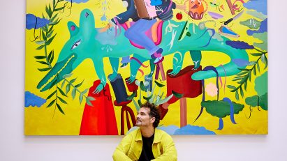 Jamie Hayon sitting in front of a painting featuring a person riding a green creature