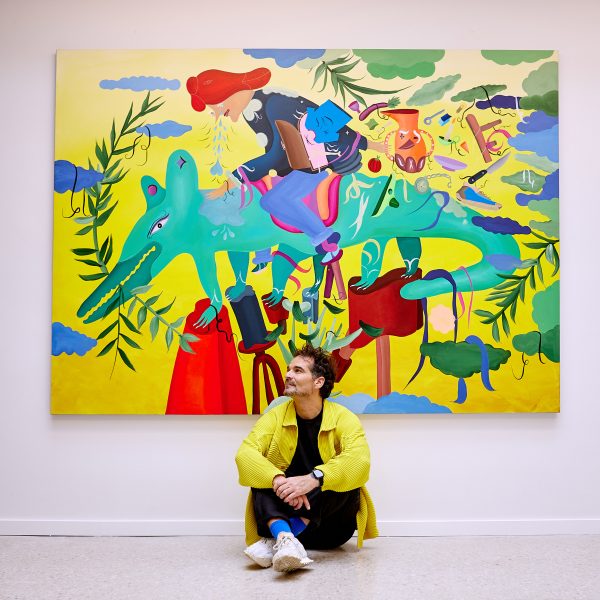 Jamie Hayon sitting in front of a painting featuring a person riding a green creature
