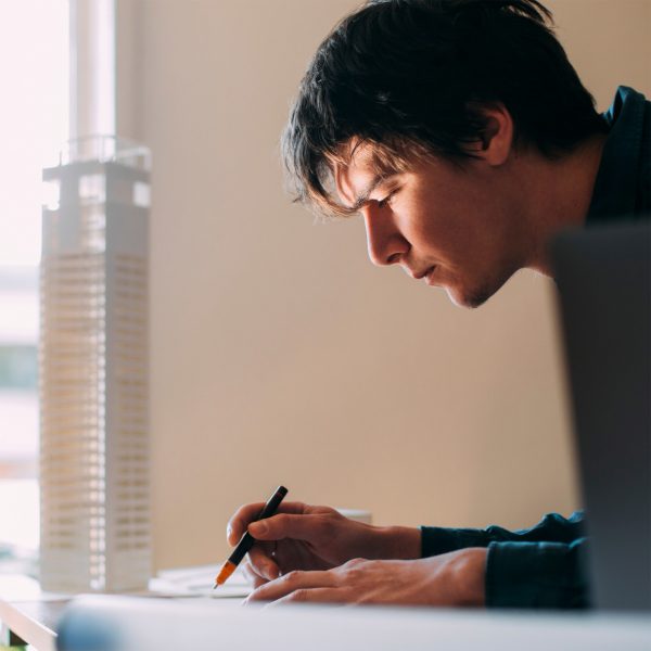 A person is writing next to a window, in front of which there is an architecture model