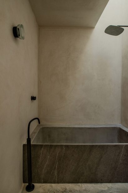 A grey stone bathtub illuminated by a skylight