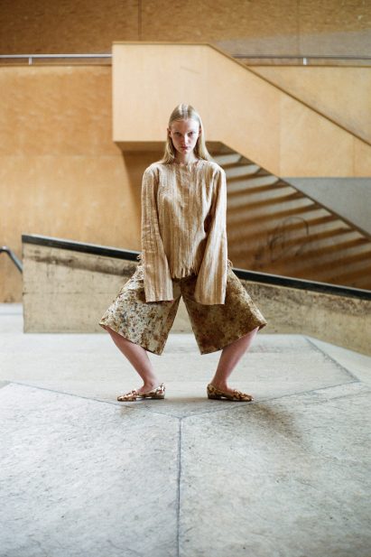 Standing model wears neutral coloured top and culotte trousers