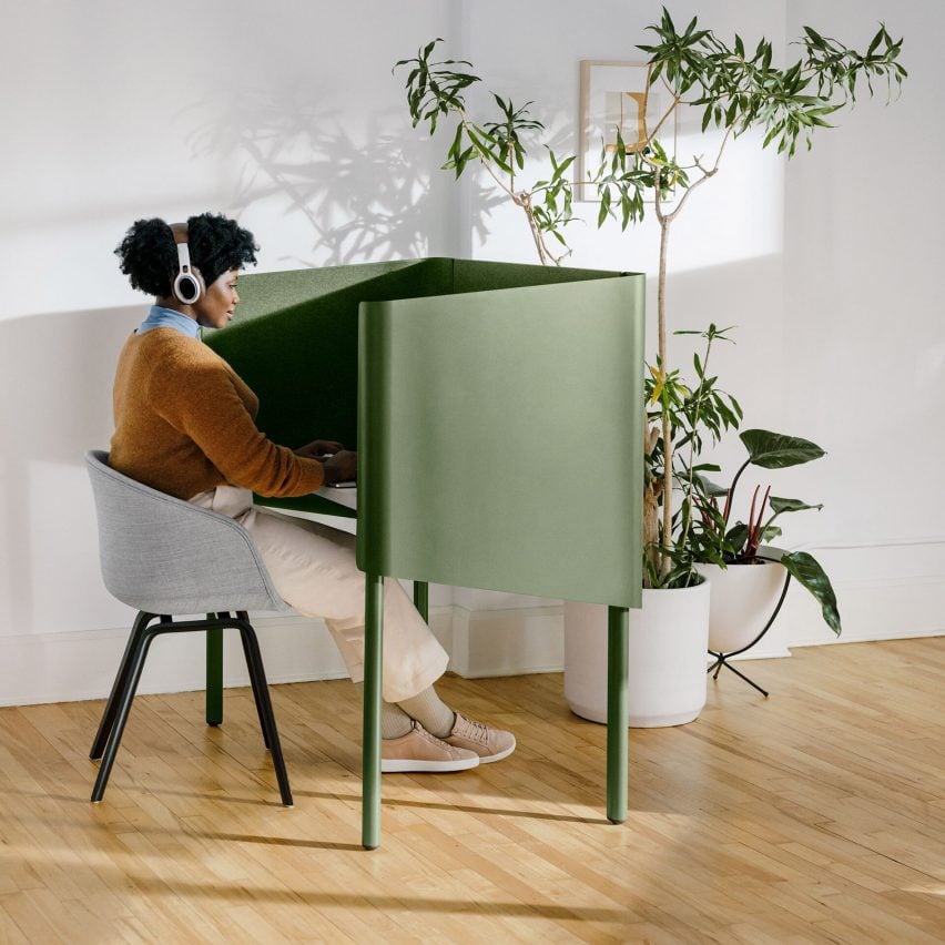 Woman sits at green enclosed desk