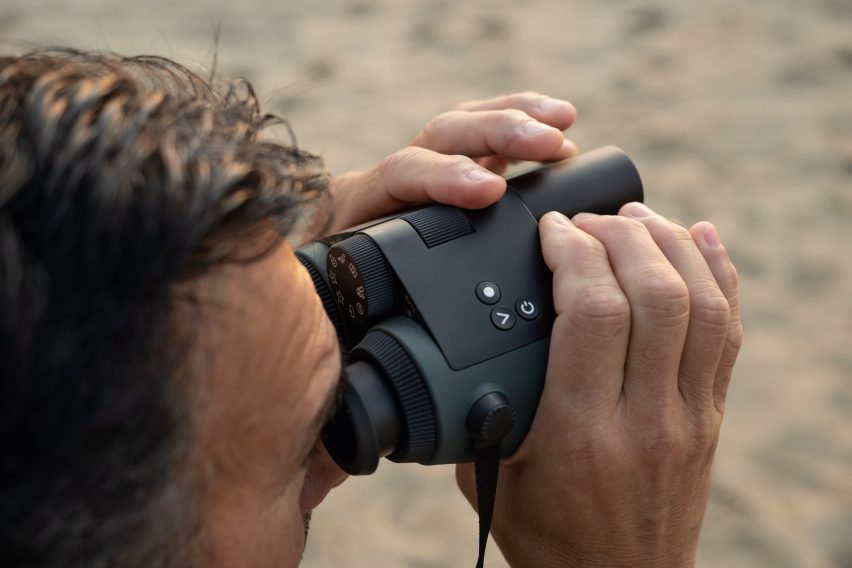 Photo of a man in close-up from over his shoulder while he looks through a large pair of binoculars