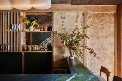 Blue-green counter with ceramic vase and flowers, in front of a wood-panelled wall