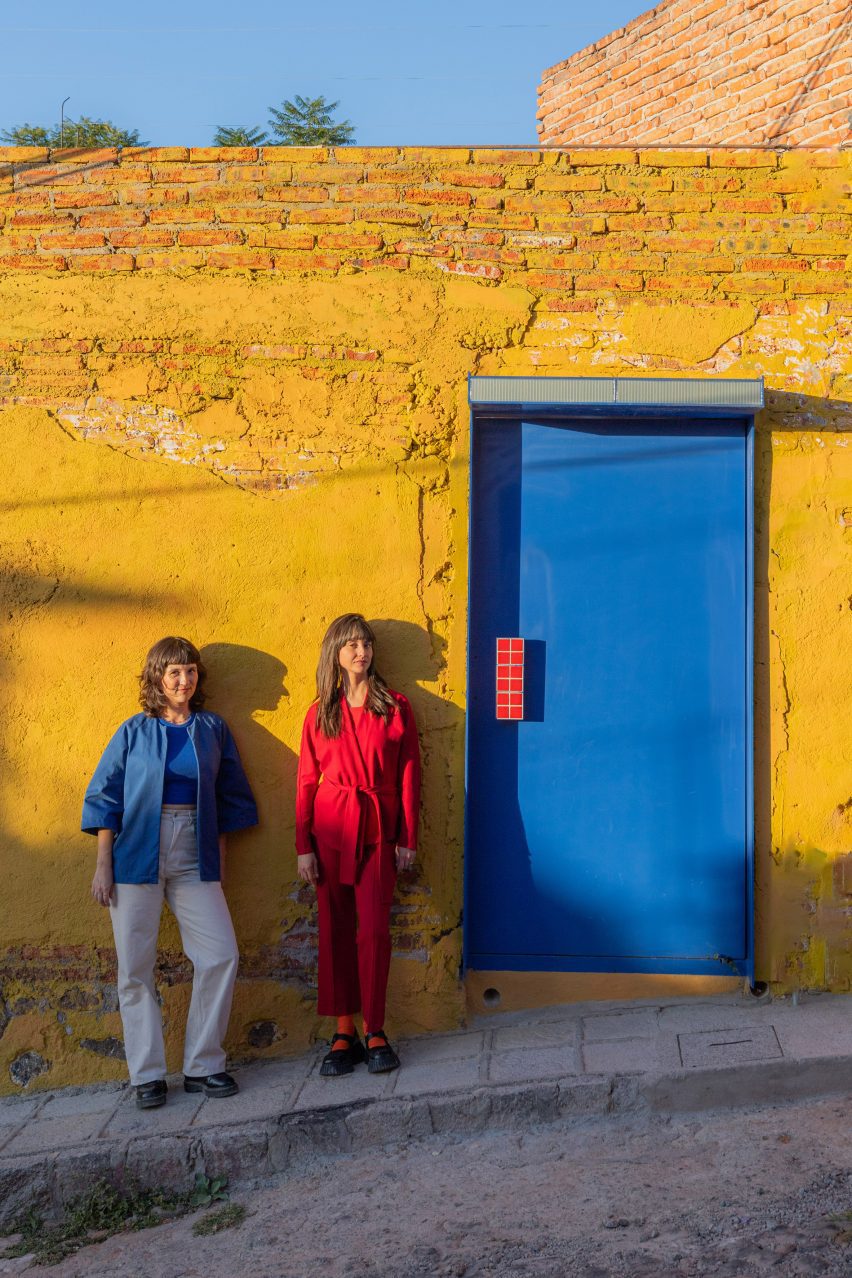 two people standing in front of a yellow wall