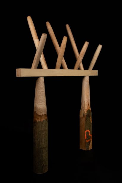 Photo of an experimental structure with roughly carved wooden columns on the bottom, a glulam beam joining them, and spindles shooting out of the beam at the top