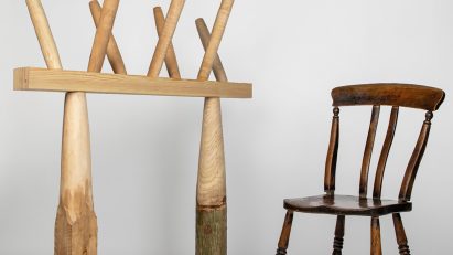 Photo of a traditional wooden chair on the right and an experimental column and beam structure topped by spindles on the left