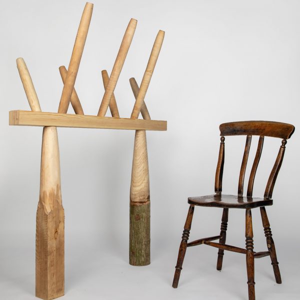 Photo of a traditional wooden chair on the right and an experimental column and beam structure topped by spindles on the left