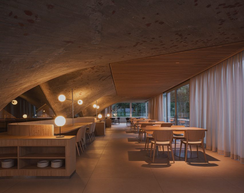 Dining tables beneath a concrete paraboloid and slatted wooden ceiling panels inside a brutalist restaurant in Spain by Zooco Estudio