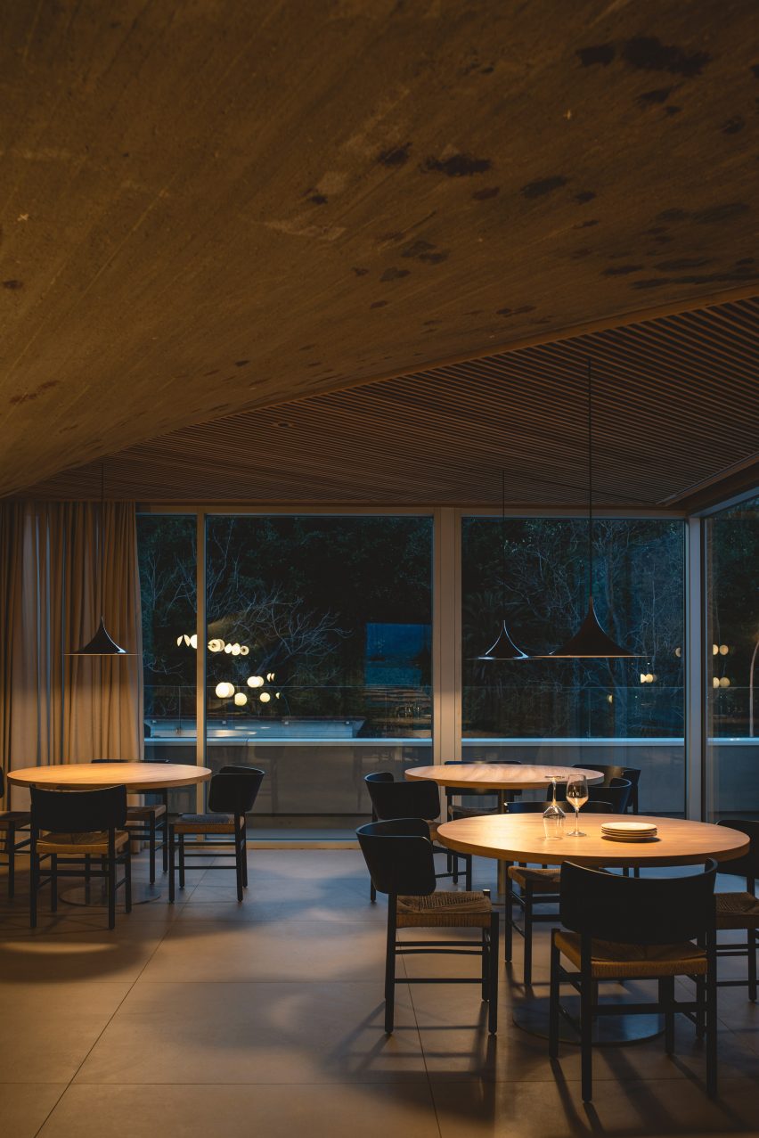 Dining tables beneath a concrete paraboloid and slatted wooden ceiling panels inside a brutalist restaurant in Spain by Zooco Estudio