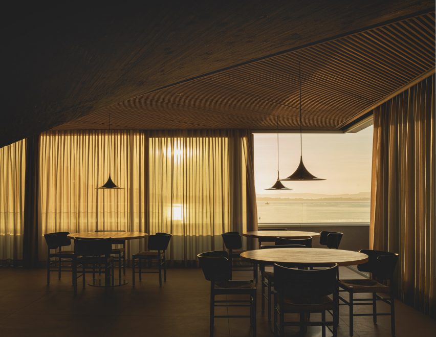 Dining tables overlooking views of the bay from a frameless corner window inside a brutalist restaurant in Spain by Zooco Estudio