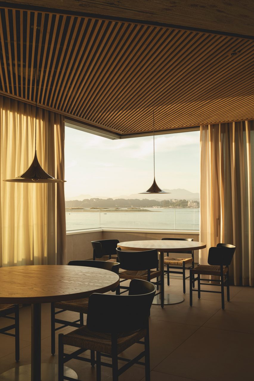 Dining tables overlooking views of the bay from a frameless corner window inside a brutalist restaurant in Spain by Zooco Estudio